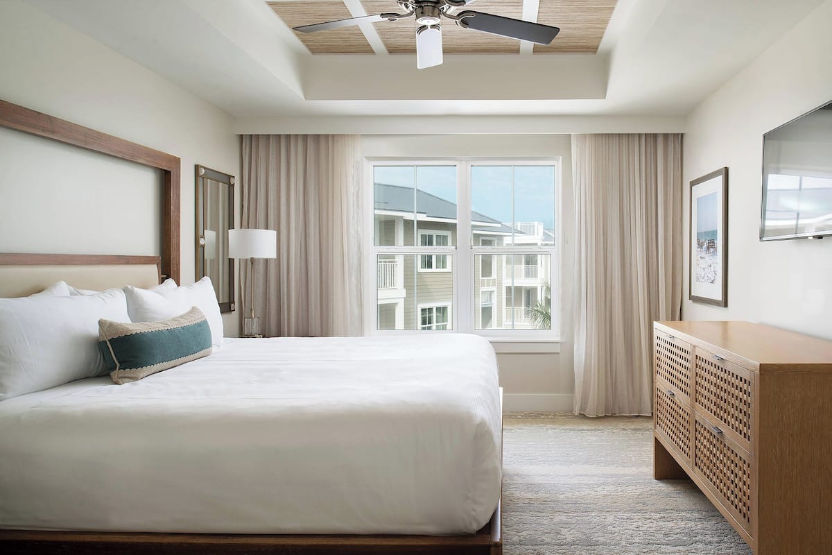 Een hotelkamer met een groot bed, een houten dressoir, een plafondventilator en een raam met gordijnen.