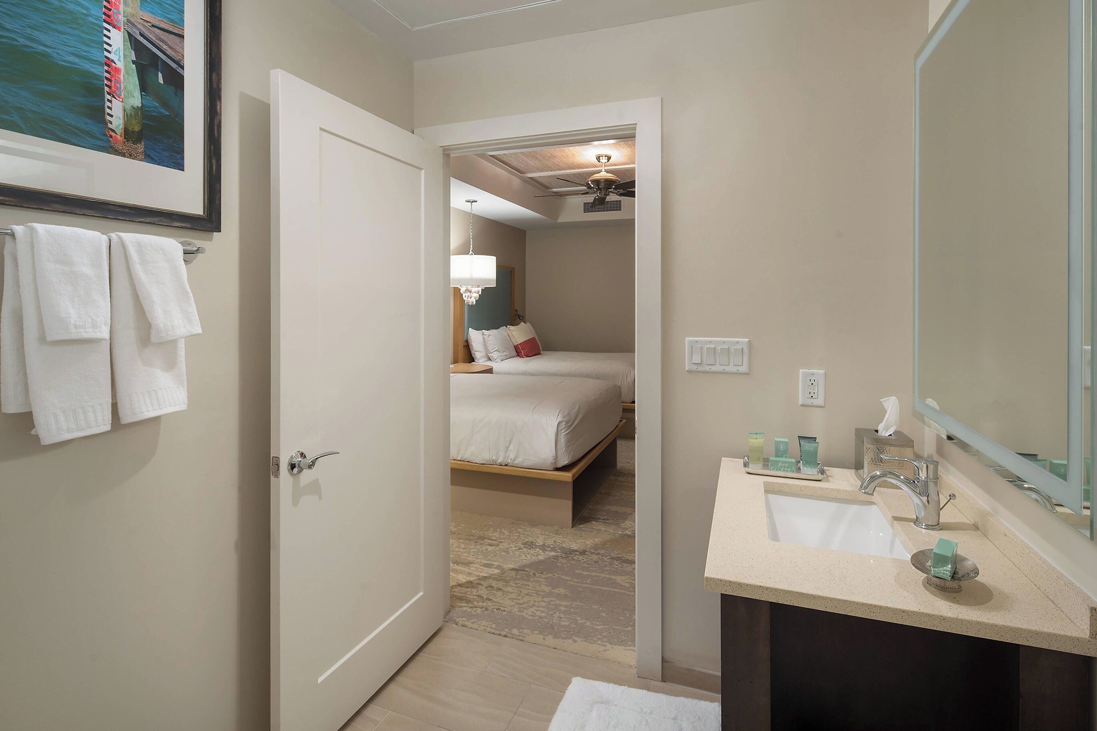 A hotel room with a bed, a bathroom with a sink and mirror, and a hallway leading to another room.