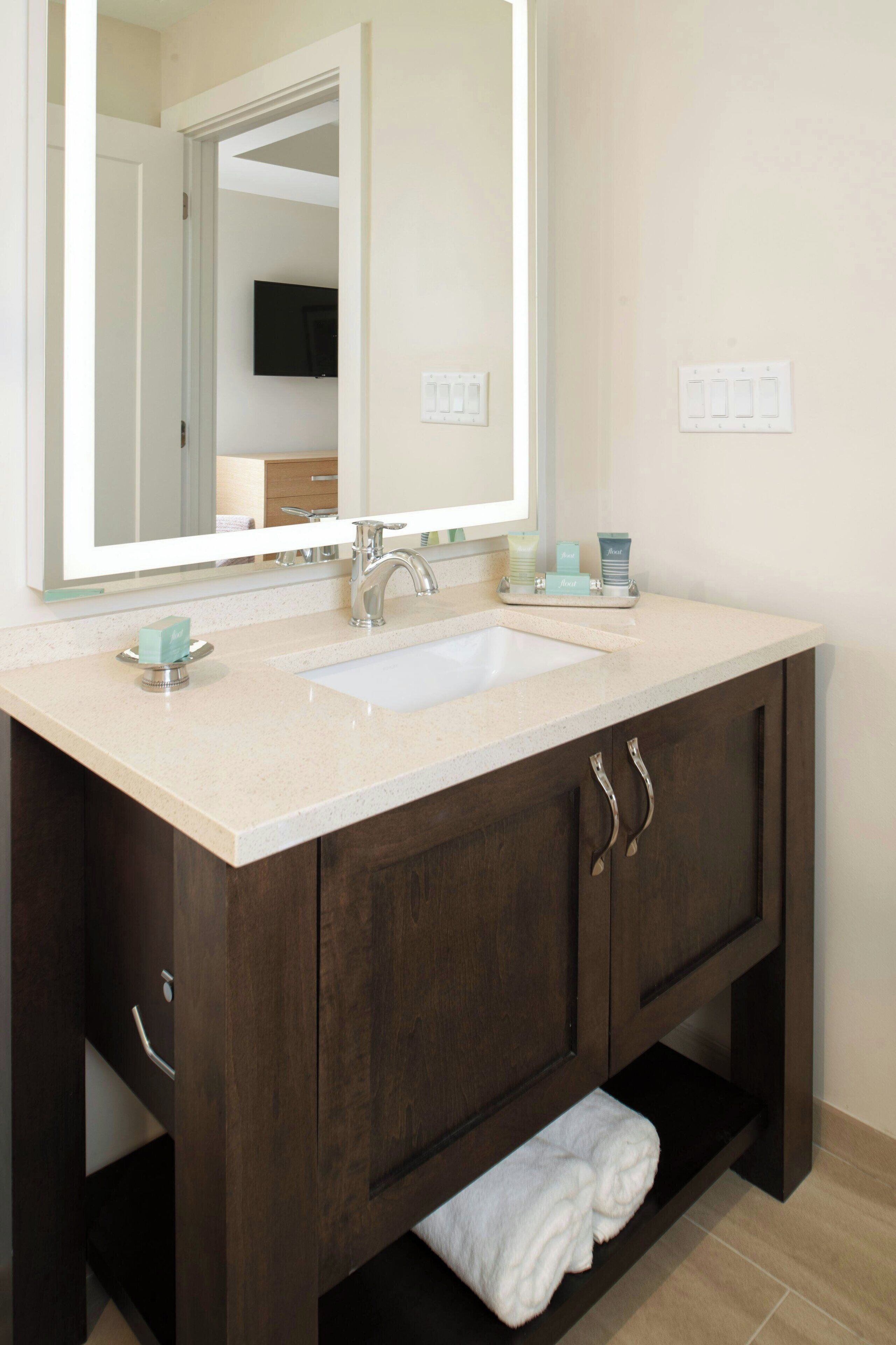 A bathroom with a double sink, dark wooden vanity, a large mirror, and a towel rack.