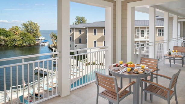 Un balcon avec une table à manger dressée pour le petit-déjeuner, offrant une vue sur une piscine et un port de plaisance.