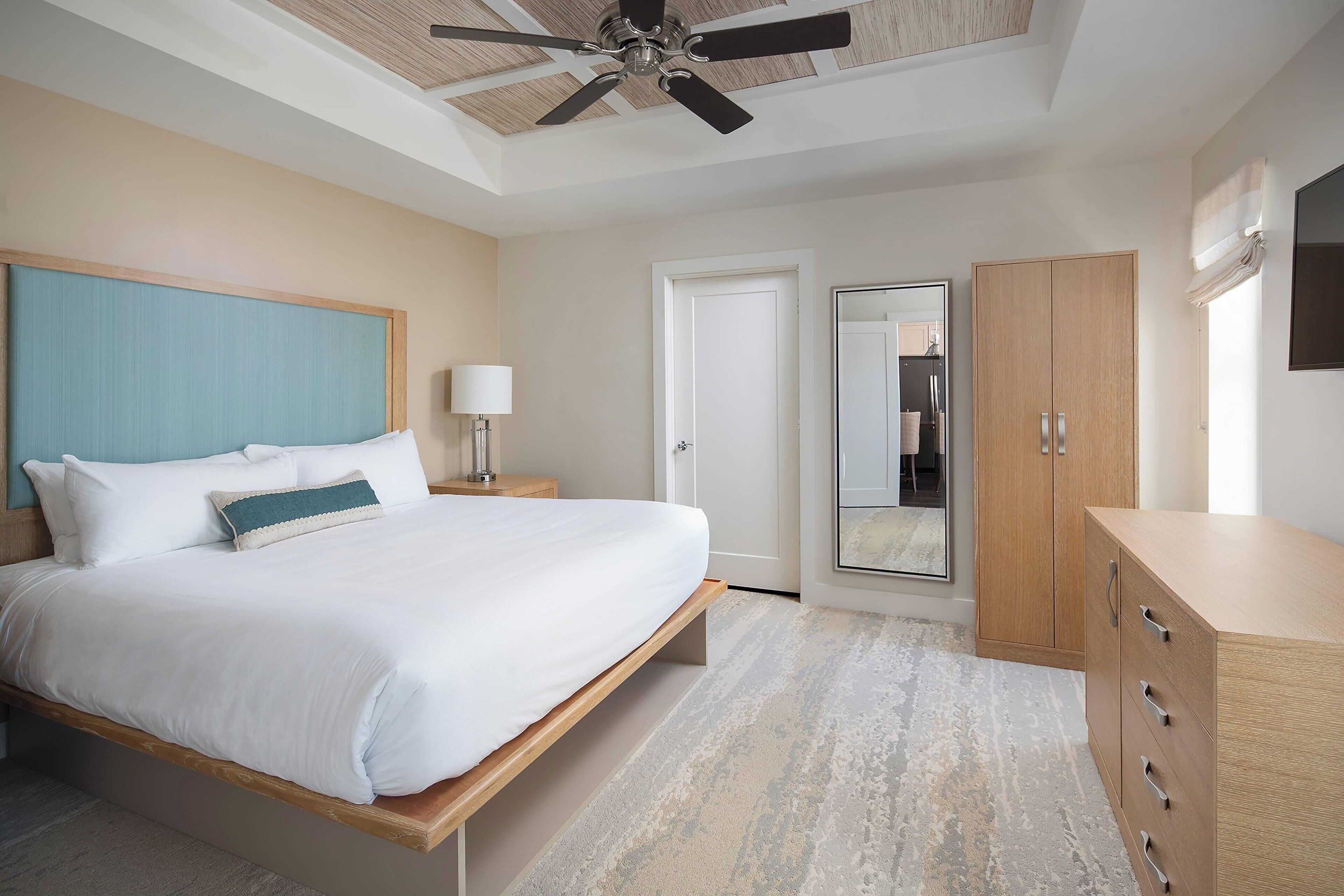 A bedroom with a bed, a ceiling fan, a wardrobe, and a door.
