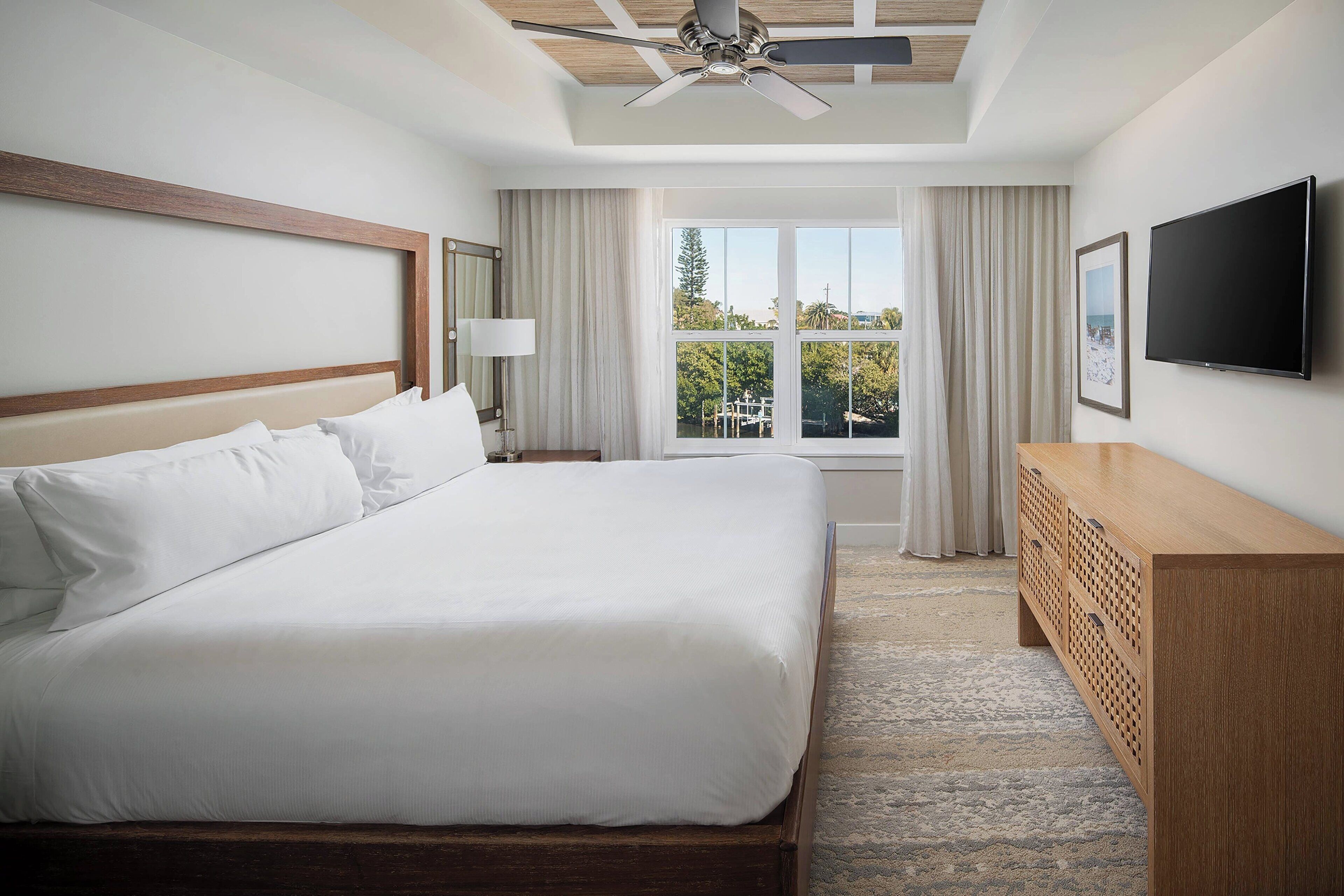 Une chambre d’hôtel avec un grand lit, un ventilateur de plafond, une télévision, une fenêtre avec des rideaux et une vue sur l’extérieur.