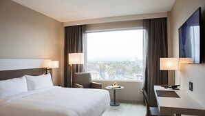 A hotel room with a large bed, a desk, two chairs, a small table, and a TV on the wall.