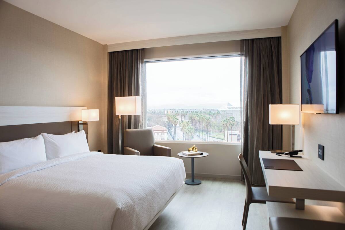 Une chambre d’hôtel avec un grand lit, un bureau, deux chaises, une petite table et un téléviseur fixé au mur.