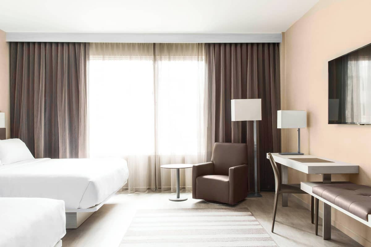 Une chambre d’hôtel avec deux lits, un bureau, une chaise et une lampe.
