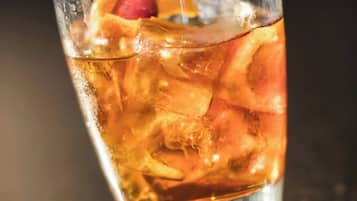 Un verre contenant une boisson glacée, une cerise et une paille, posé sur une surface réfléchissante, avec une serviette en dessous.
