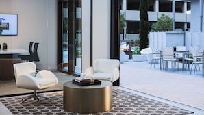 Eine moderne Hotellobby mit einer Rezeption, einer Sitzecke mit weißen Stühlen, einem runden Couchtisch und einem gemusterten Teppich.