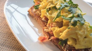A slice of toast topped with scrambled eggs and greens on a white plate.