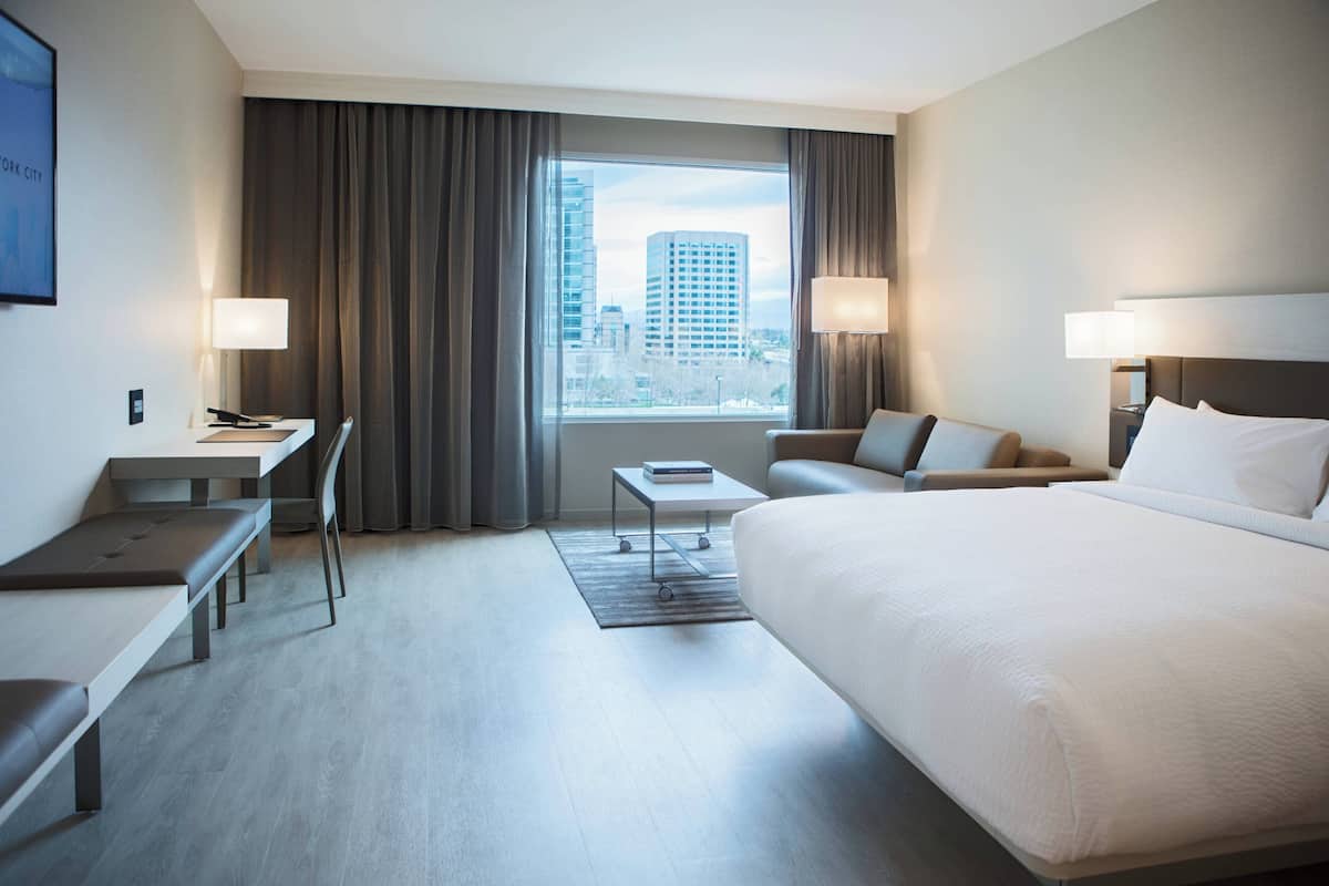 Une chambre d’hôtel avec un grand lit, un bureau, une chaise, une petite table et une vue sur la ville.