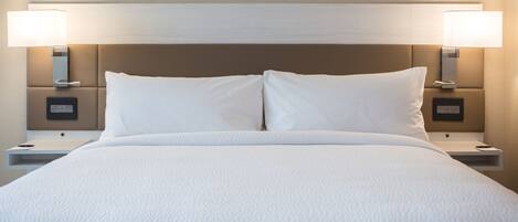 A neatly made bed with white linens, two bedside lamps, and a modern headboard.