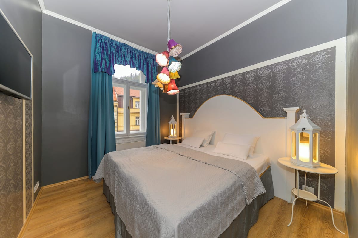 Een slaapkamer met een bed, nachtkastje, hanglamp en een raam met gordijnen.