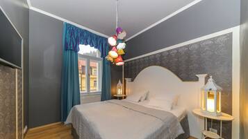 Une chambre à coucher avec un lit, une table de chevet, une lampe suspendue et une fenêtre avec des rideaux.