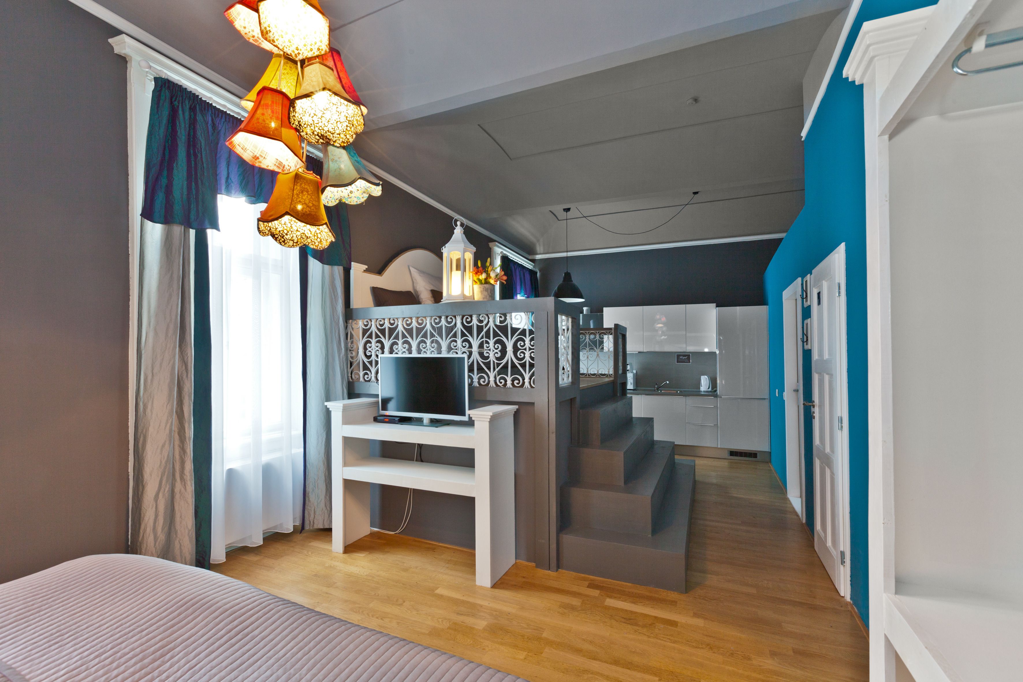 Ein modernes Hotelzimmer mit Bett, Fernseher auf einem weißen Schrank, Küchenzeile und einer Treppe zu einer weiteren Ebene.