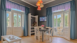 Una habitación con mesa de comedor, sillas, televisión y balcón con cortinas.