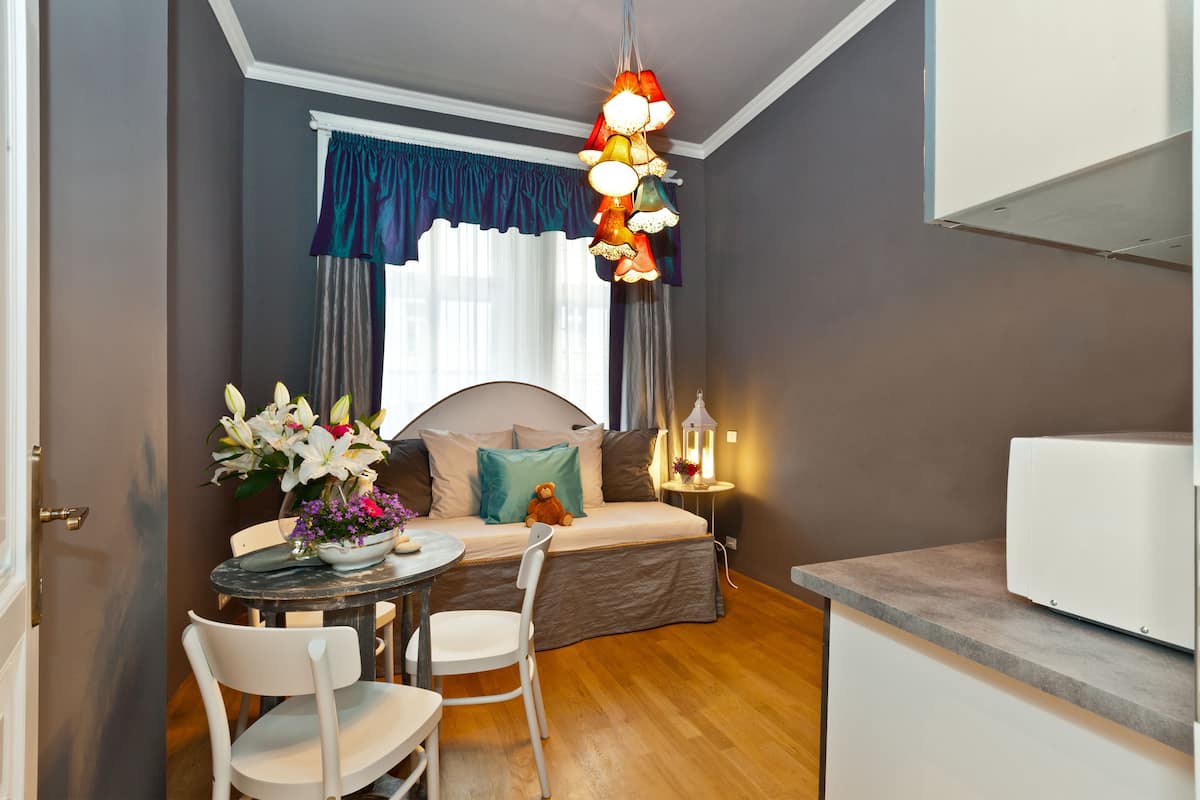 Een kleine kamer met een bed, nachtkastje, lamp en een eethoek met stoelen en een tafel.