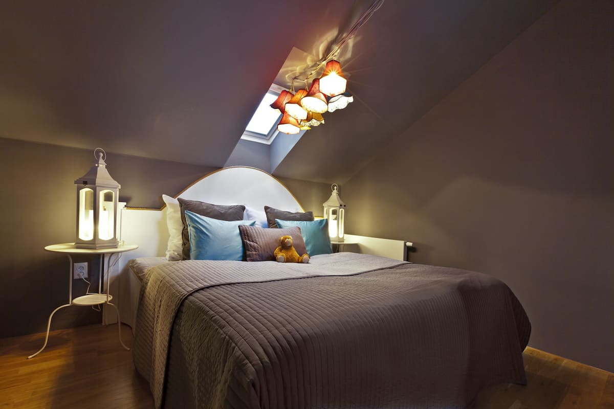 Een slaapkamer met een schuine plafond, een bed met hoofdeinde, twee nachtkastjes en een dakraam.