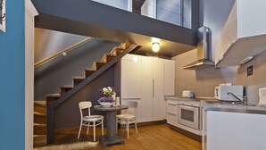 Una cocina moderna con una escalera de madera, armarios blancos y un comedor con dos sillas y una mesa.