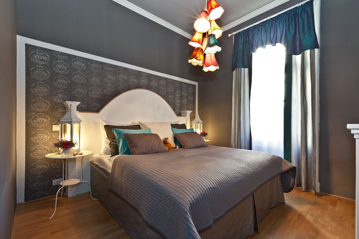 Een slaapkamer met een groot bed, twee nachtkastjes, een wandlamp en een raam met gordijnen.