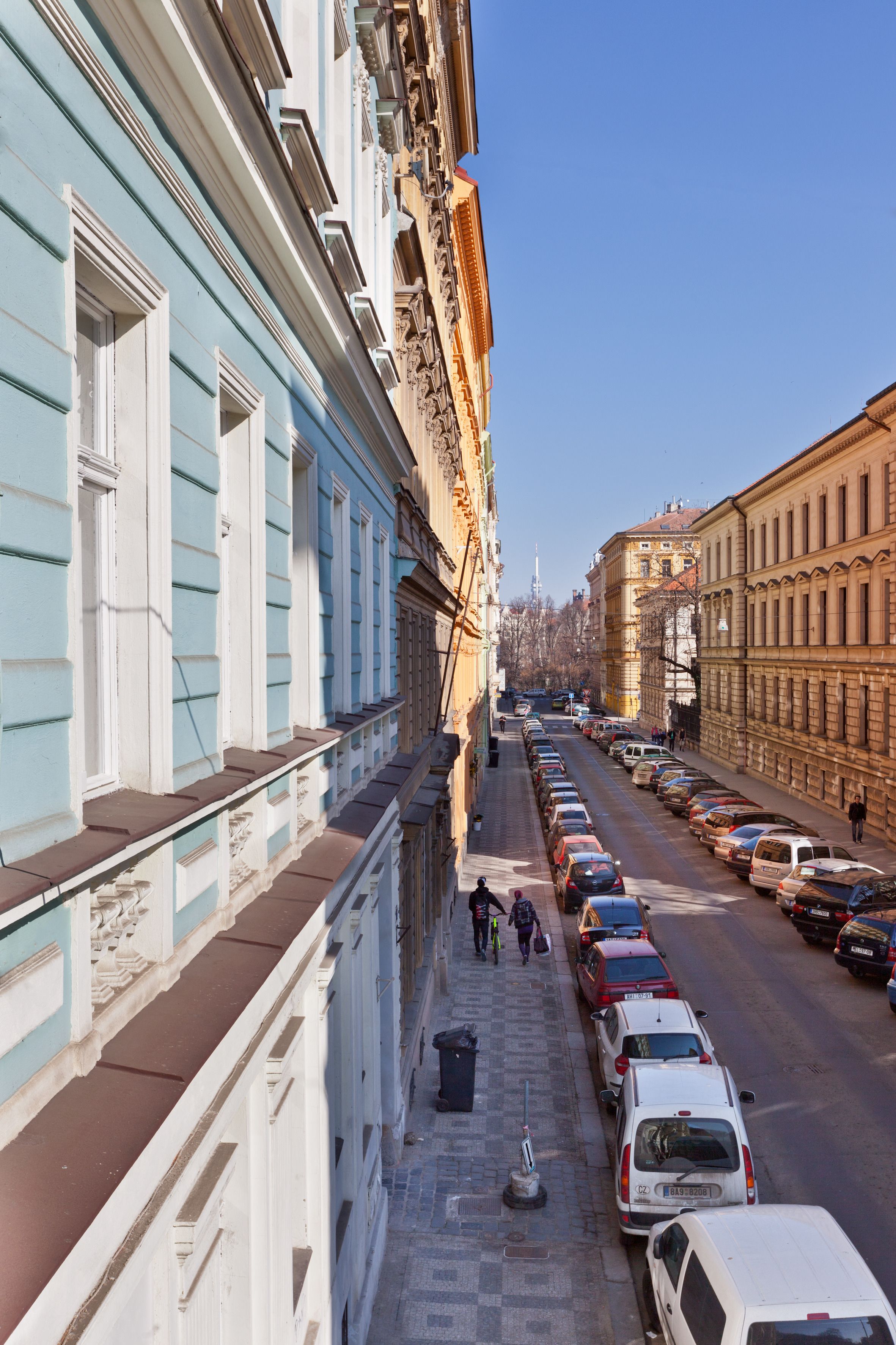 Straßenansicht mit parkenden Autos, Gebäuden im klassischen Stil und blauem Himmel.
