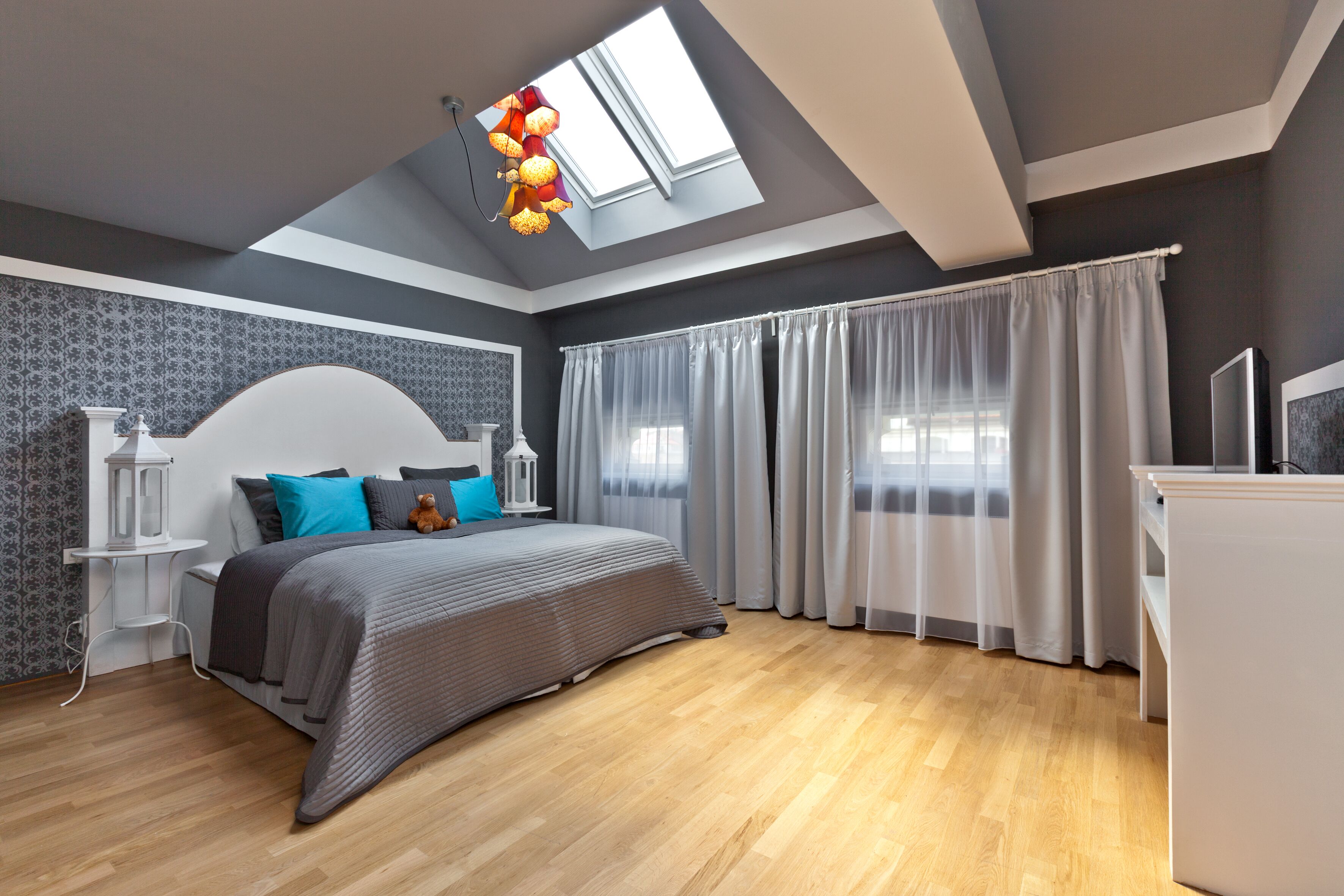 Een moderne slaapkamer met dakraam, een bed met grijze beddengoed, een nachtkastje en een bureau.