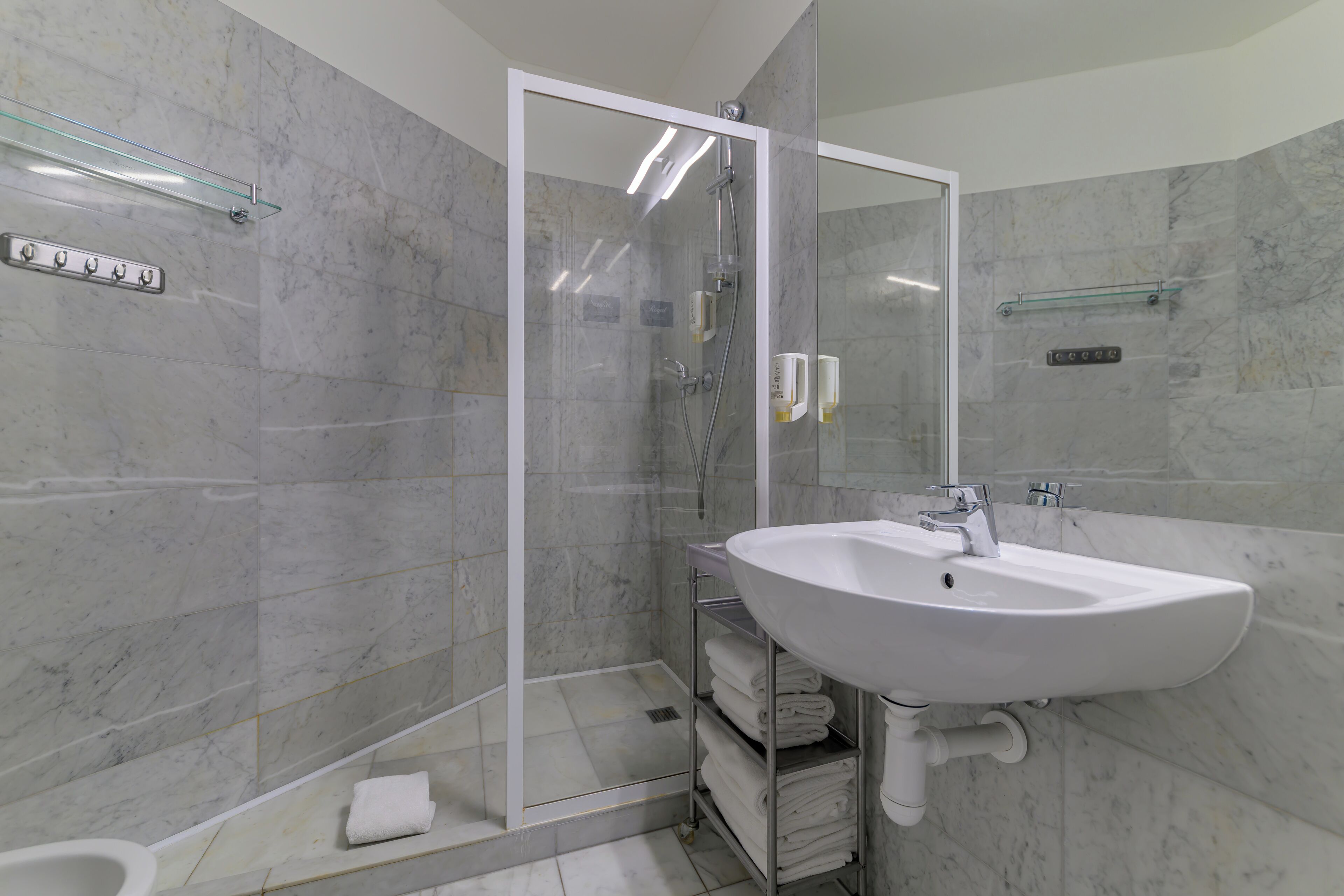 Ein modernes Badezimmer mit einer gläsernen Duschkabine, einem weißen Waschbecken und Marmorwänden.