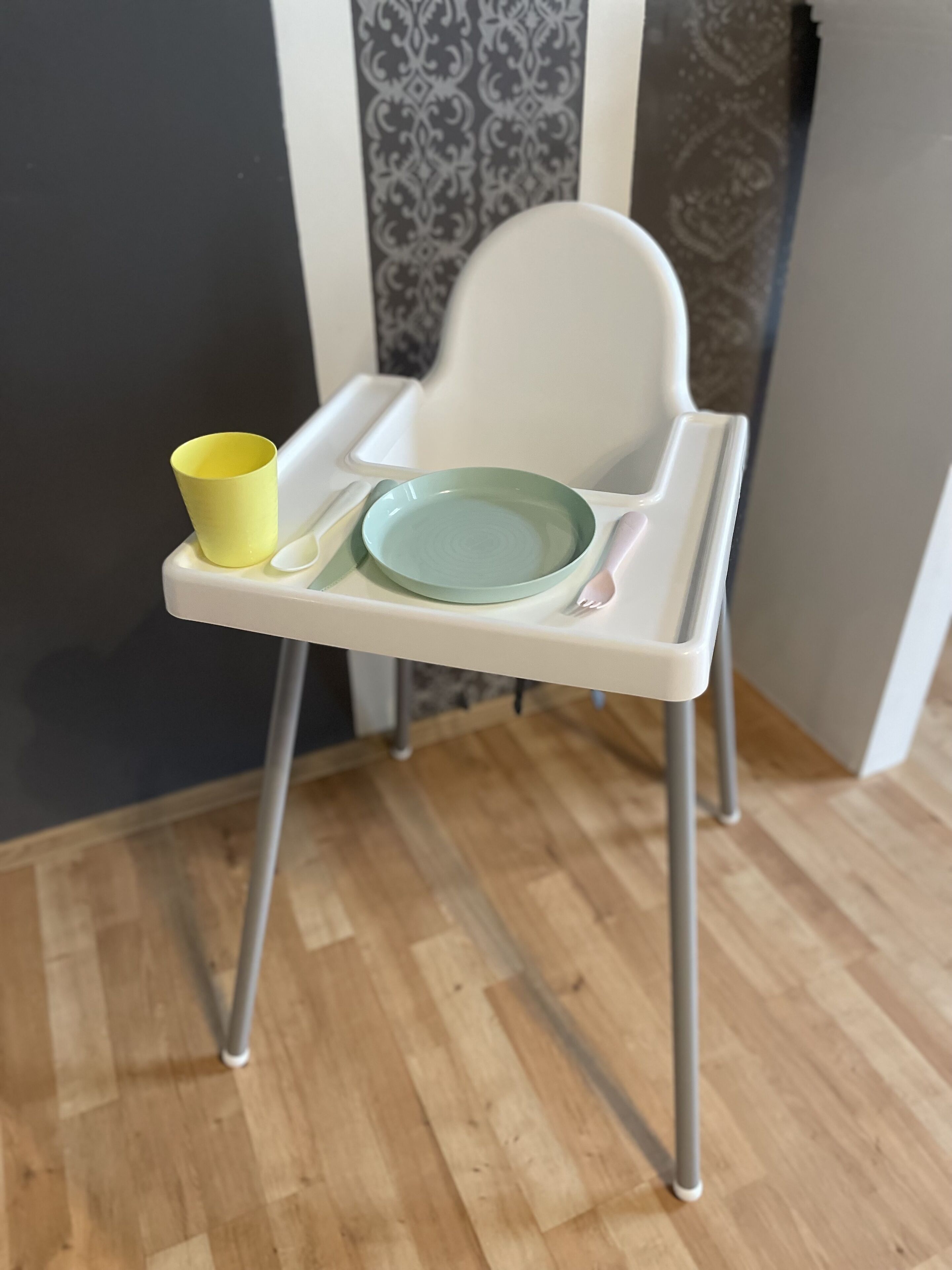 Una silla alta con mesita, sosteniendo un plato verde y una taza amarilla.