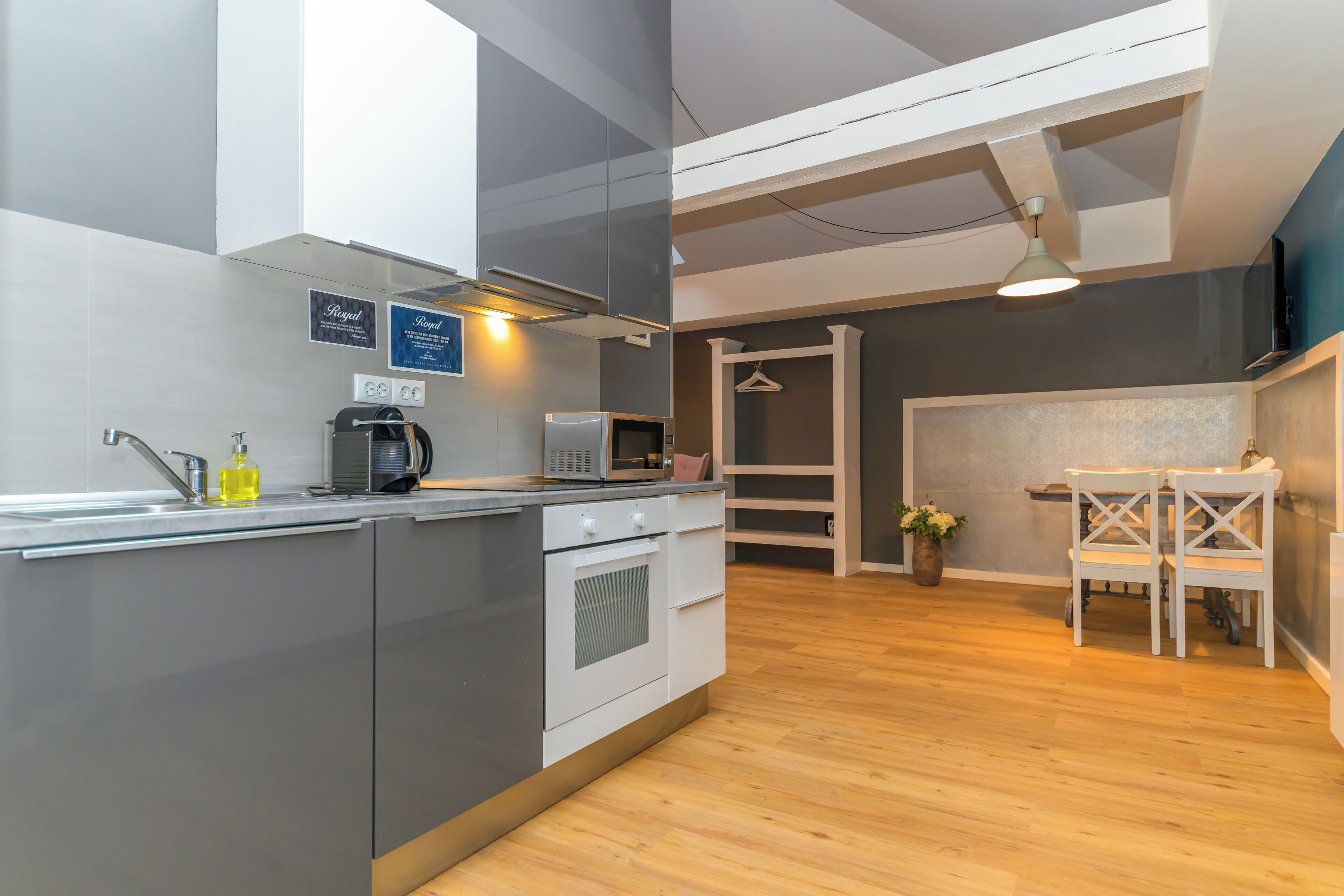 A modern kitchen with grey cabinets, a built-in oven, and a microwave. There is a wooden dining table with chairs and a hanging light fixture above.