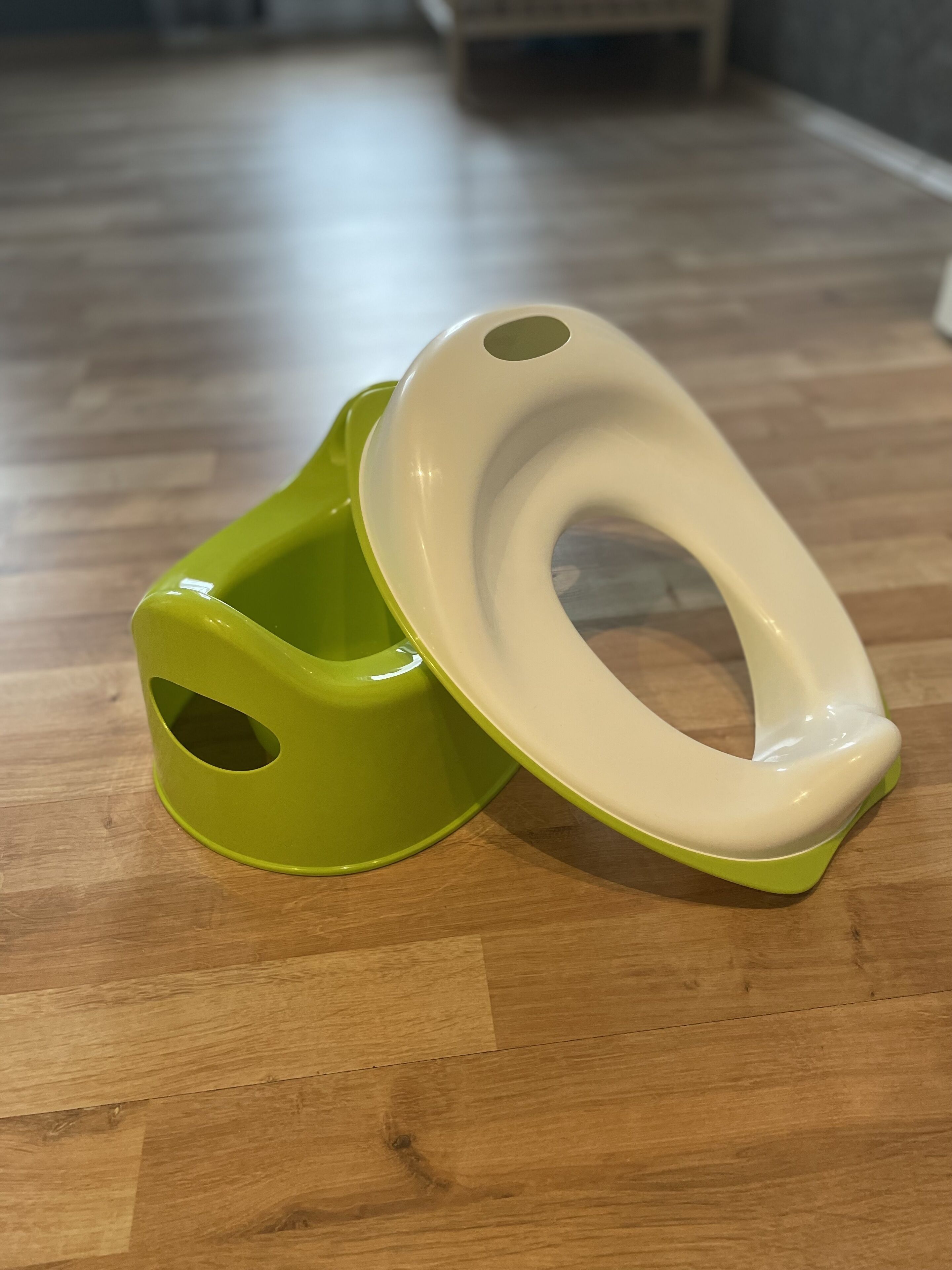 A toilet with a green seat and lid on a wooden floor.