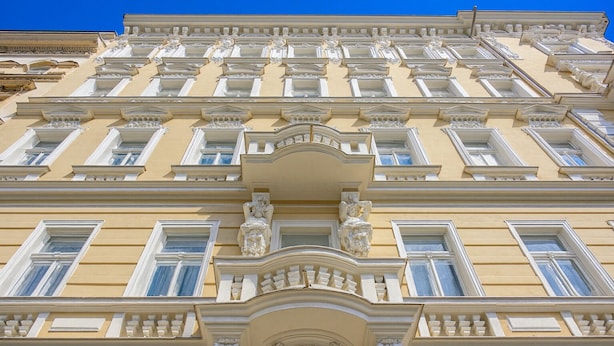 Fachada de edificio con detalles arquitectónicos clásicos, incluyendo marcos de ventanas ornamentados y molduras decorativas.