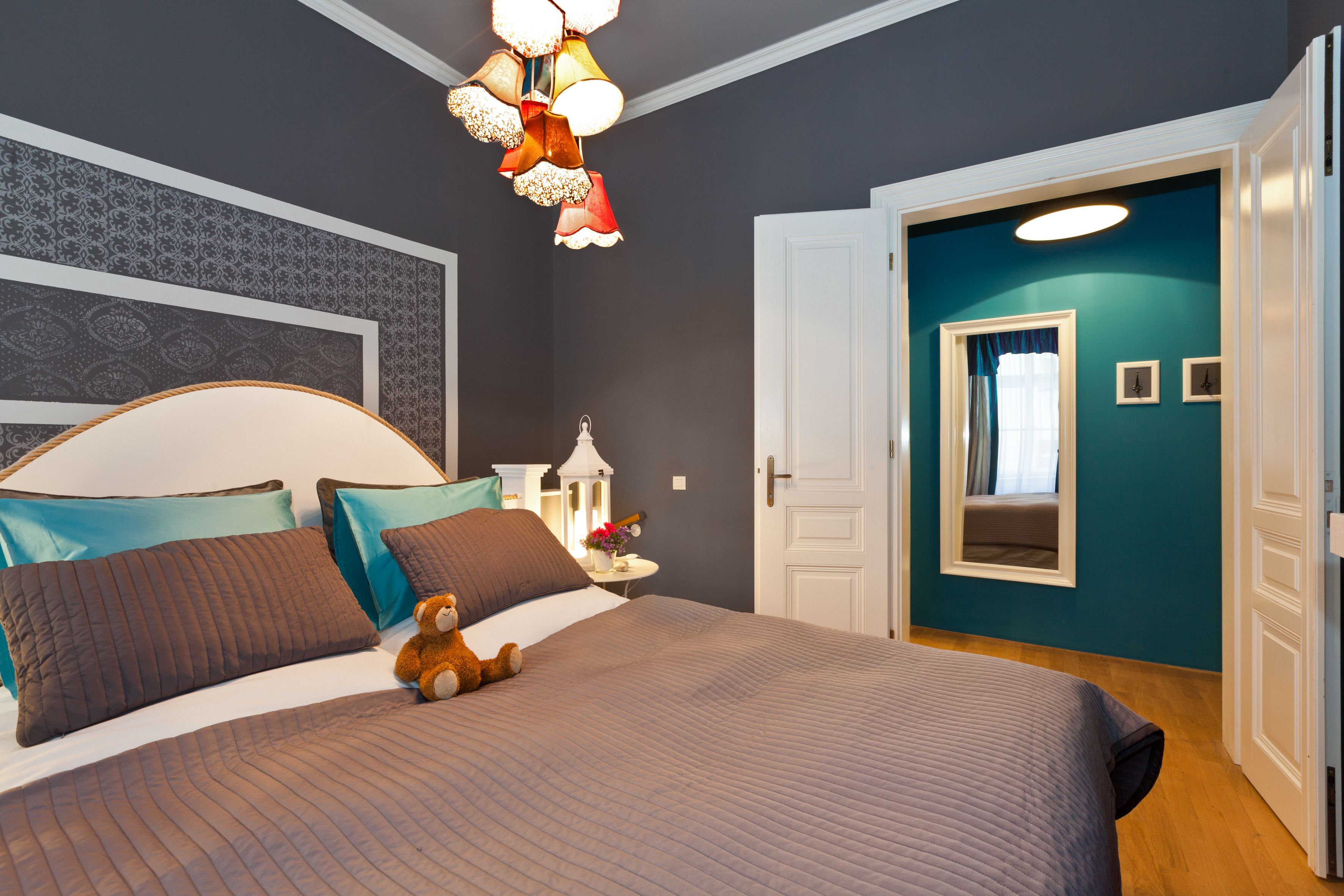 Un dormitorio con una cama grande, un osito de peluche, una mesita de noche y una puerta que da a otra habitación.