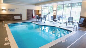 An indoor swimming pool with clear water, surrounded by chairs and a lifeguard stand.