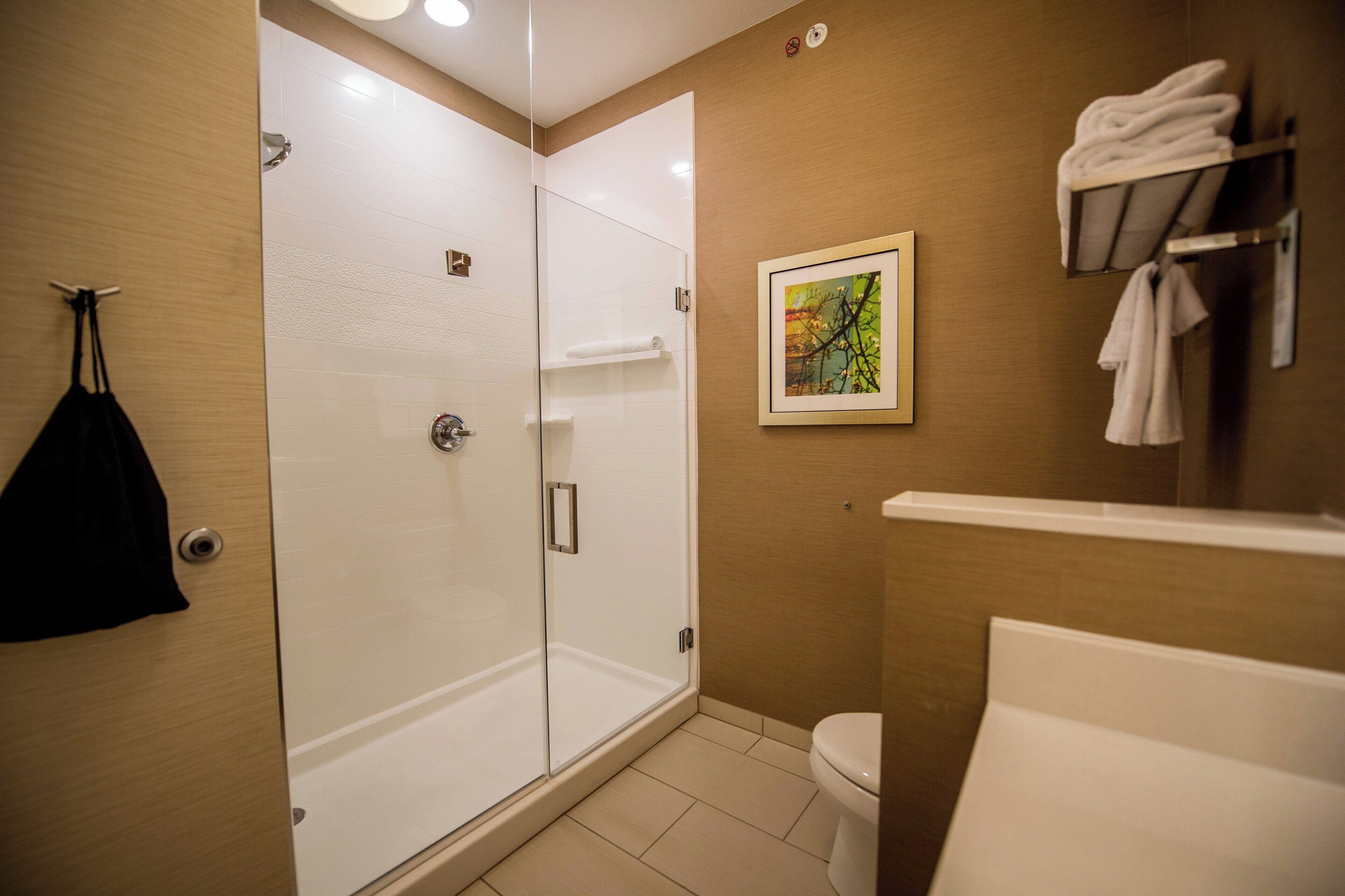 A modern bathroom with a glass-enclosed shower, a toilet, and a towel rack with folded towels.
