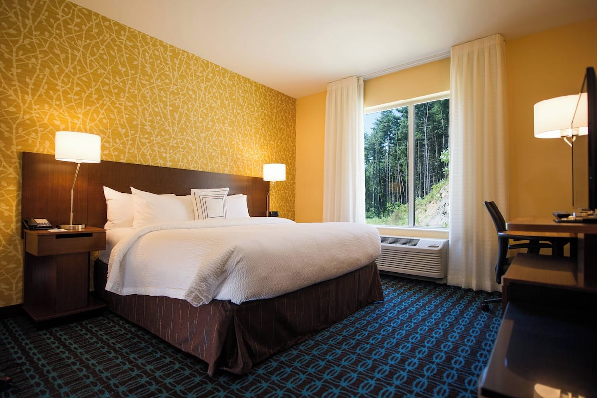 A hotel room with a large bed, two bedside tables with lamps, a desk, and a window with curtains.