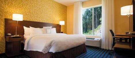 Habitación de hotel con una cama grande, dos mesitas de noche con lámparas, un escritorio y un ventanal con cortinas.