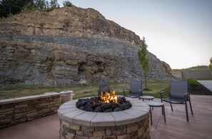 Un espacio de estar al aire libre con un hogar de piedra, dos sillones y una mesita.