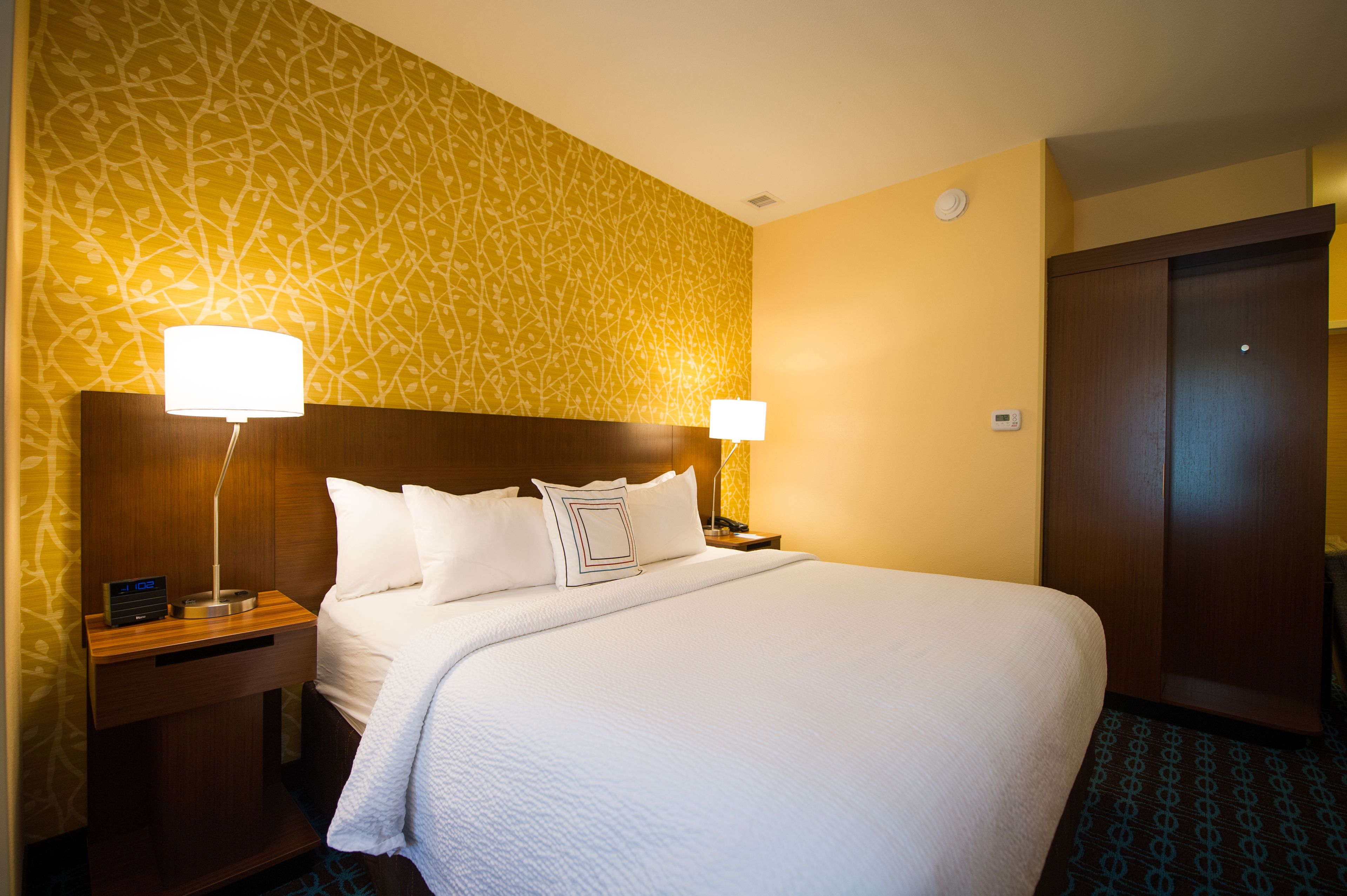 A hotel room with a large bed, two bedside tables with lamps, a wooden headboard, and a patterned wall.