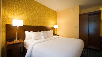 A hotel room with a large bed, two bedside tables with lamps, a wooden headboard, and a patterned wall.