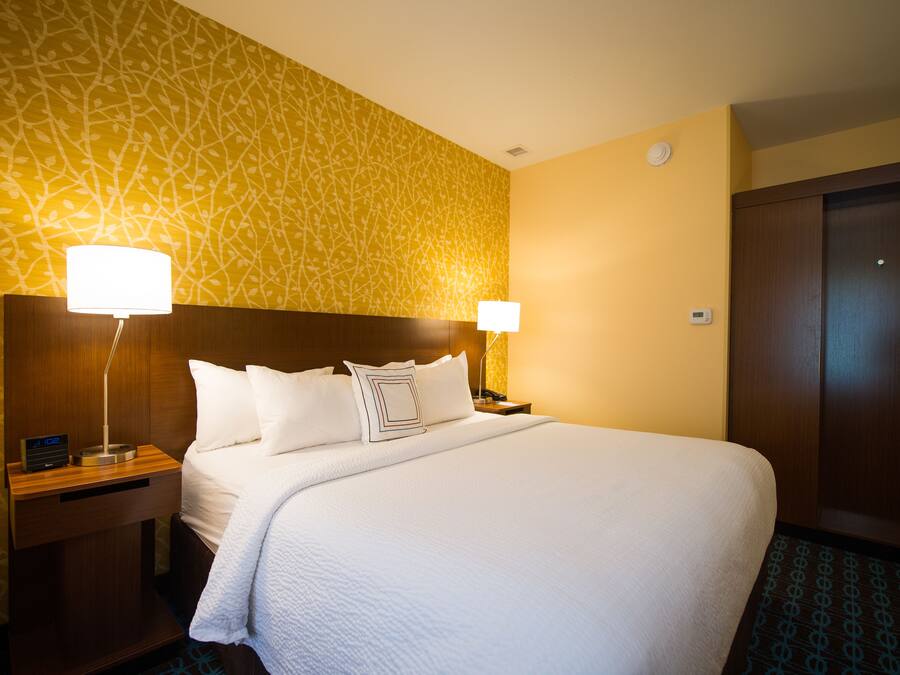 A hotel room with a large bed, two bedside tables with lamps, a wooden headboard, and a patterned wall.