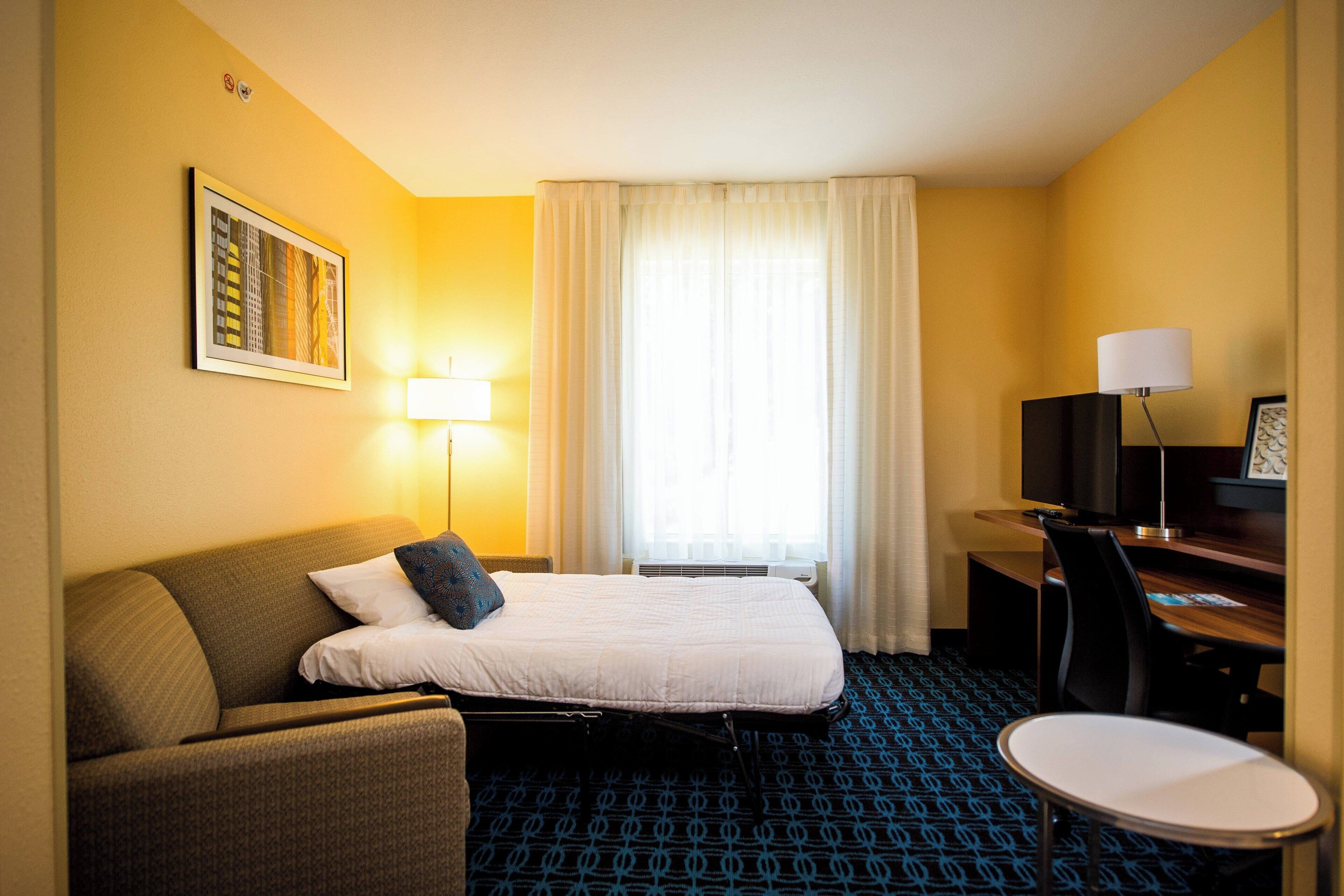 A hotel room with a bed, a sofa, a desk, a chair, a lamp, and a television.