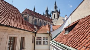 A narrow street with buildings featuring red-tiled roofs and a church with multiple spires in the background. - Cathedral Prague Apartments (Prague)