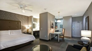 A hotel room with a bed, a desk, a chair, a round table, a sofa, and a ceiling fan. - Homewood Suites by Hilton Dallas Arlington South (Arlington)