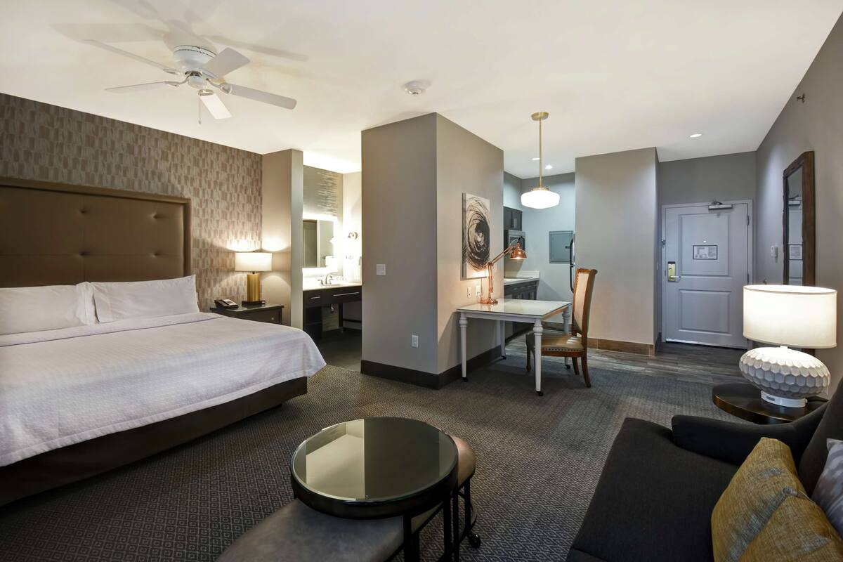 Une chambre d’hôtel comprenant un lit, un bureau, une chaise, une table ronde, un canapé et un ventilateur de plafond.