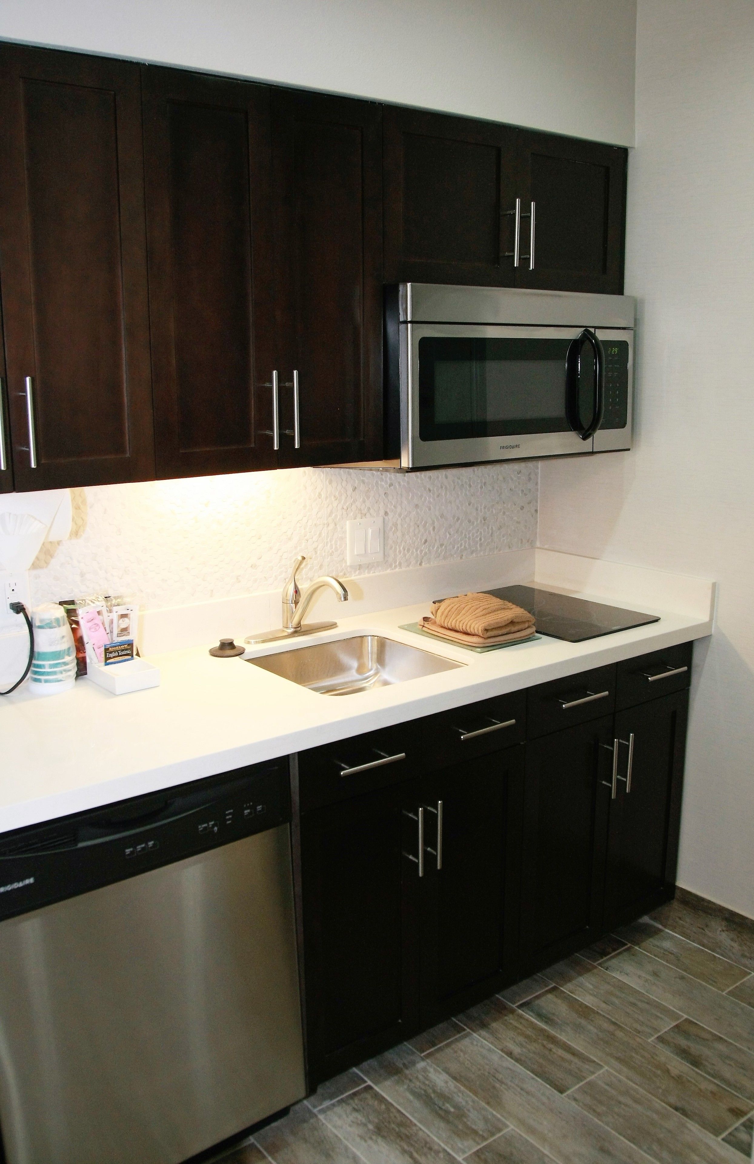 A kitchen with dark cabinets, a stainless steel dishwasher, a microwave, and a sink.