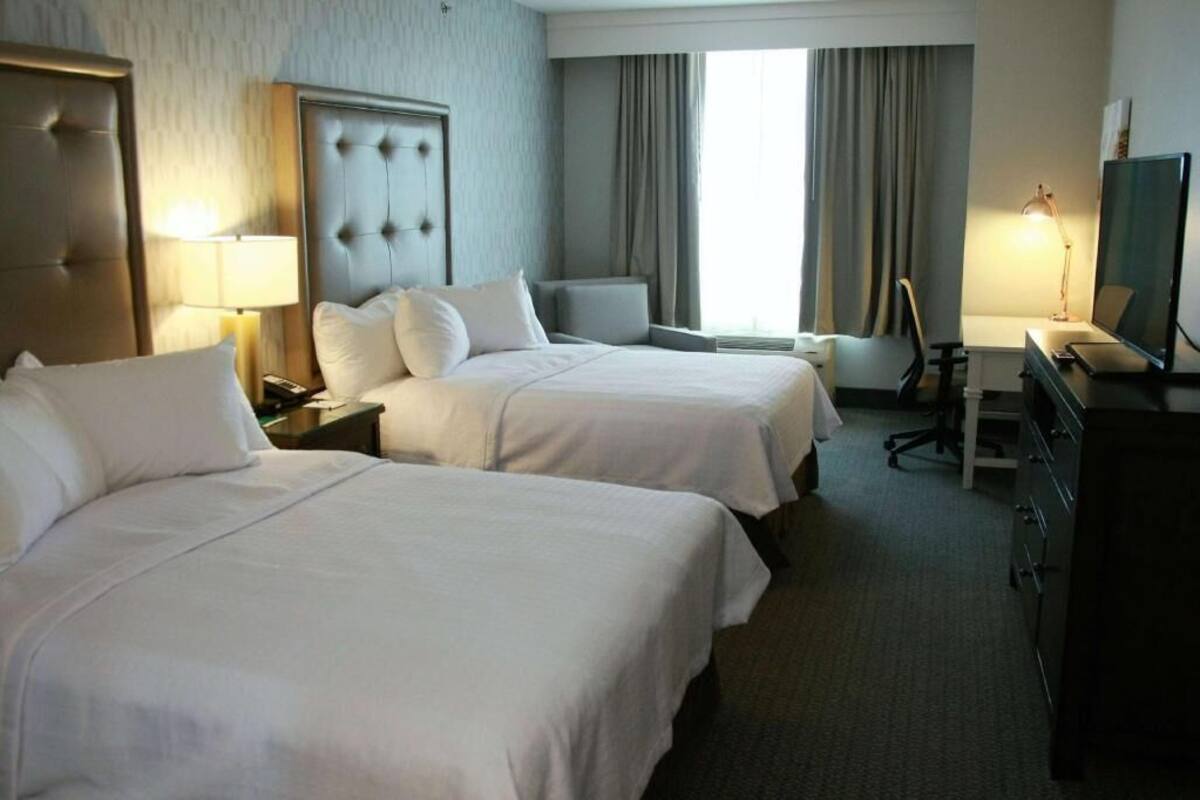 Une chambre d’hôtel avec deux lits, un bureau, une chaise, une télévision et une fenêtre avec des rideaux.