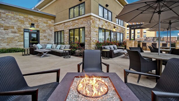 An outdoor patio with a fire pit, seating, and a building with stone facade and large windows. - Homewood Suites by Hilton Dallas Arlington South (Arlington)