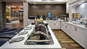 A modern kitchen with a buffet setup, including a long counter with food items and utensils. - Homewood Suites by Hilton Dallas Arlington South (Arlington)