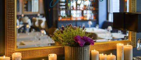 A mirror with a gold frame reflecting a bar area with candles and a potted plant.