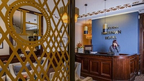 Een receptie met een houten toonbank, een receptioniste en een blauwe muur met de naam van het hotel.