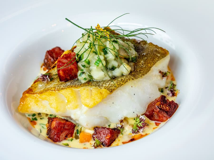 Un plat composé de poisson, de pommes de terre et de diverses garnitures, servi dans une assiette blanche.