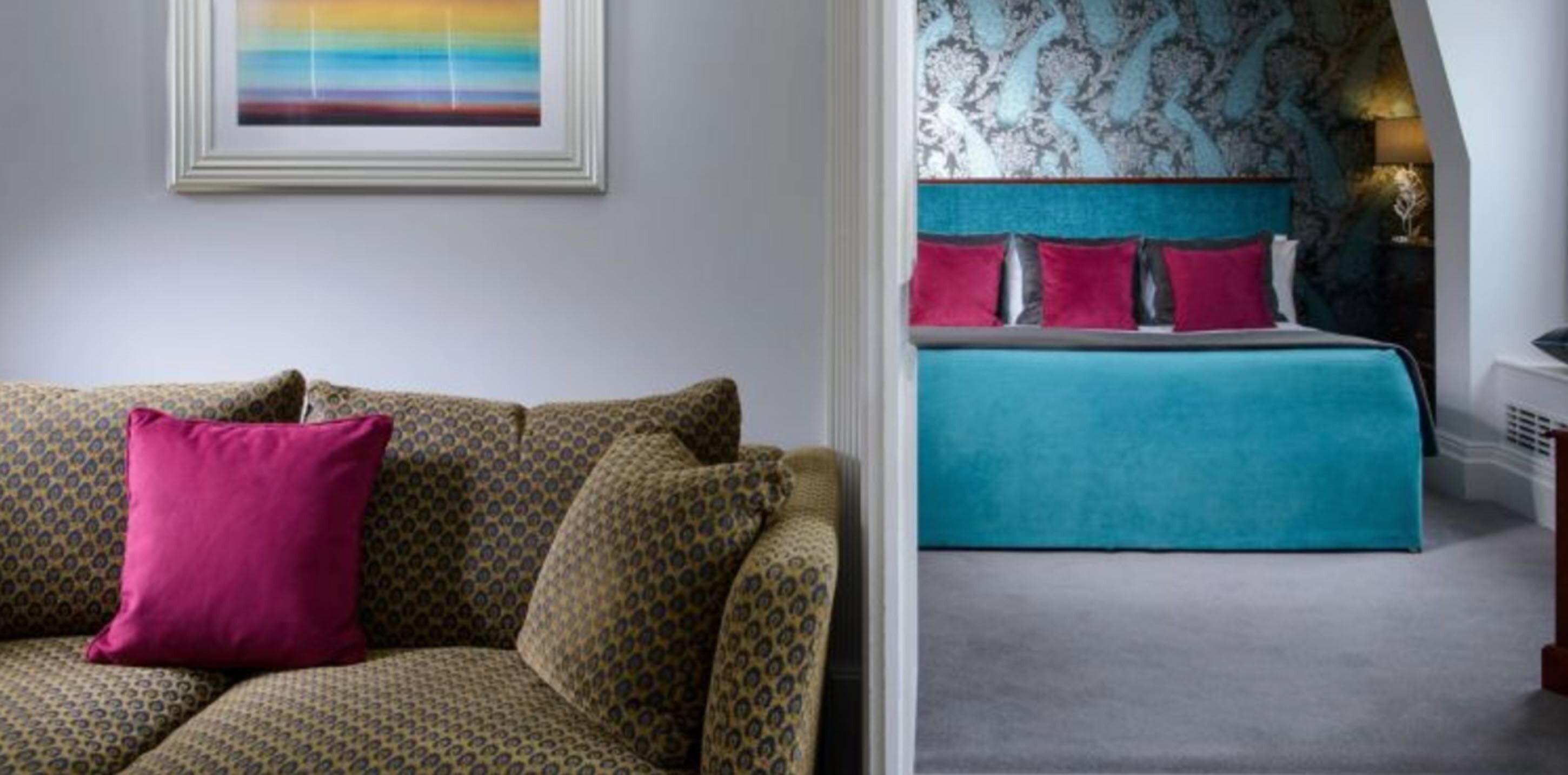 Une pièce avec un canapé à motifs, un lit avec une literie de couleur turquoise et un tableau abstrait coloré accroché au mur.